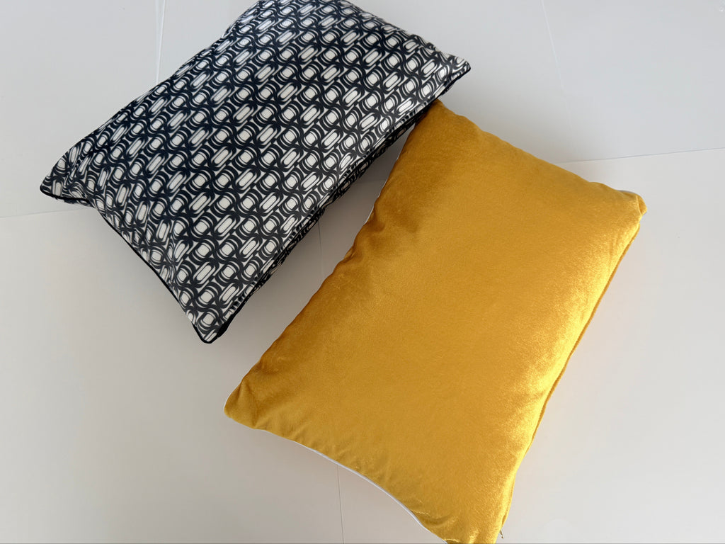 Two pillows, one black and white patterned and one mustard yellow, on a light gray background.