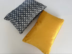 Two pillows, one black and white patterned and one mustard yellow, on a light gray background.