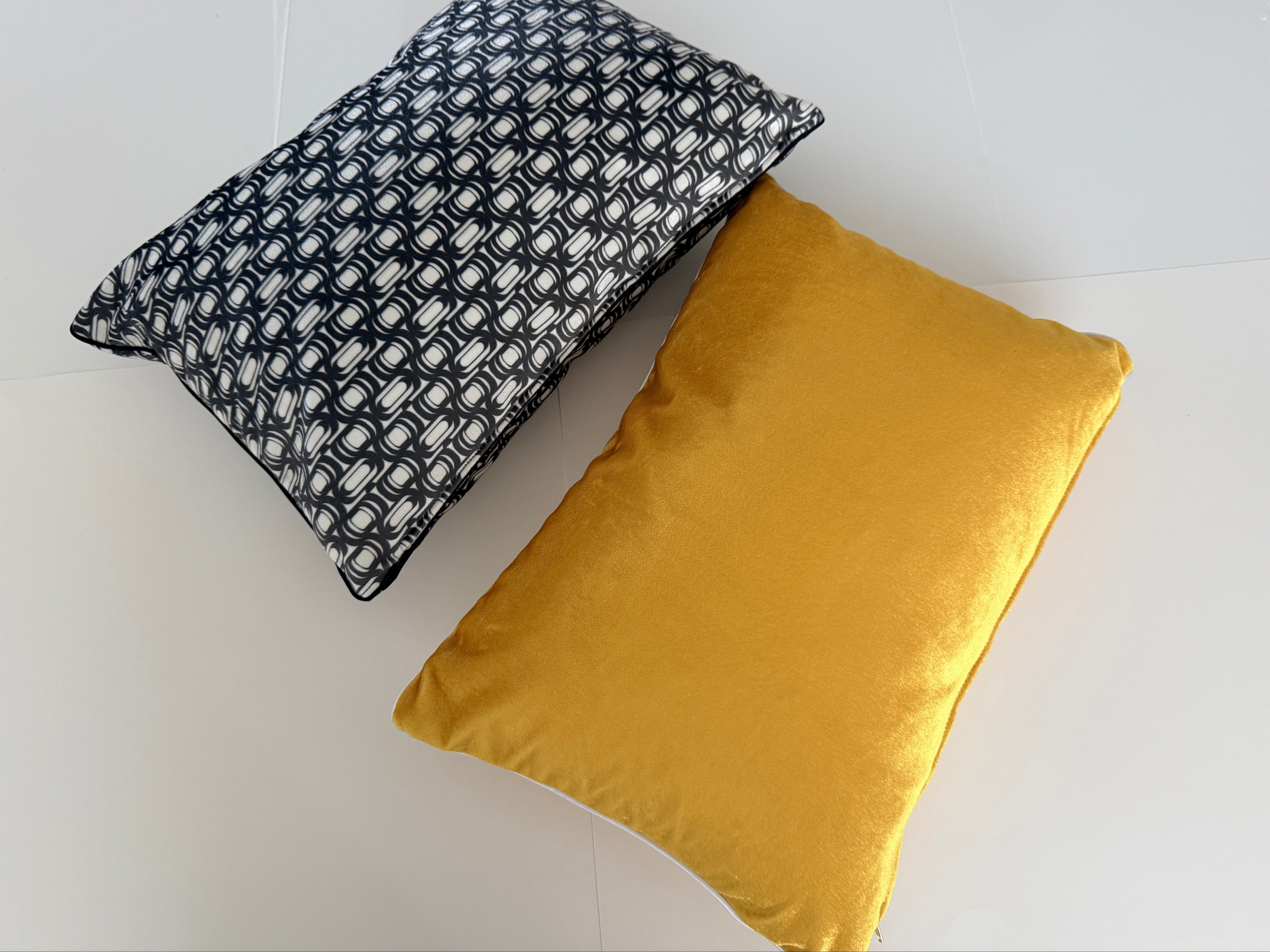 Two pillows, one black and white patterned and one mustard yellow, on a light gray background.