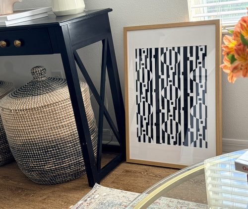 Framed geometric art piece on a wall next to a decorative vase and table.