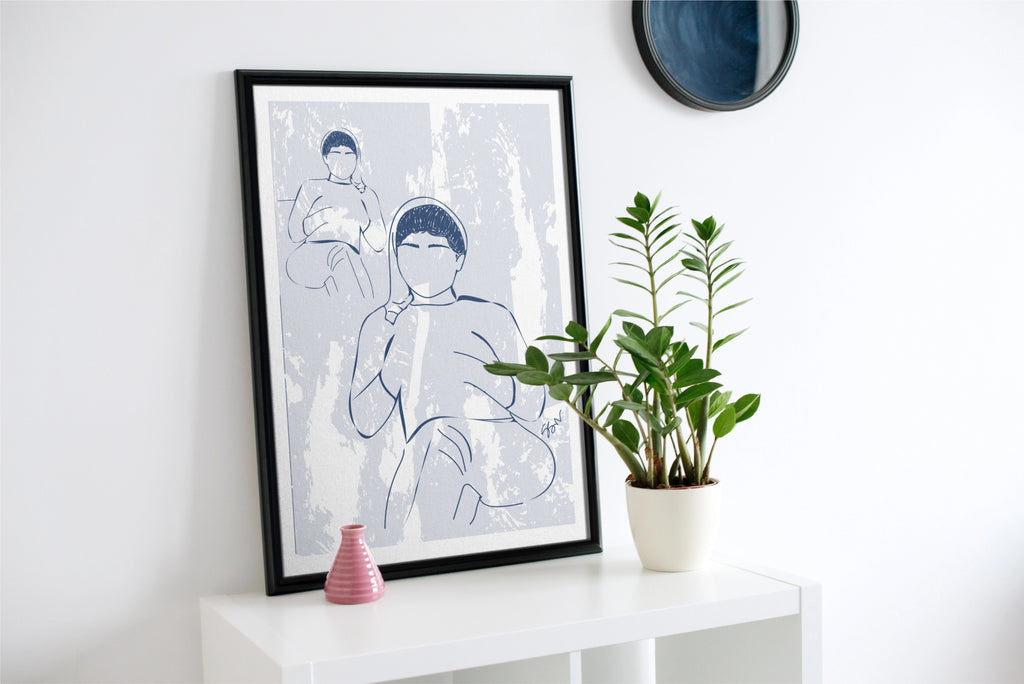 Framed artwork of a person with a child on a white wall above a white console table with a plant.