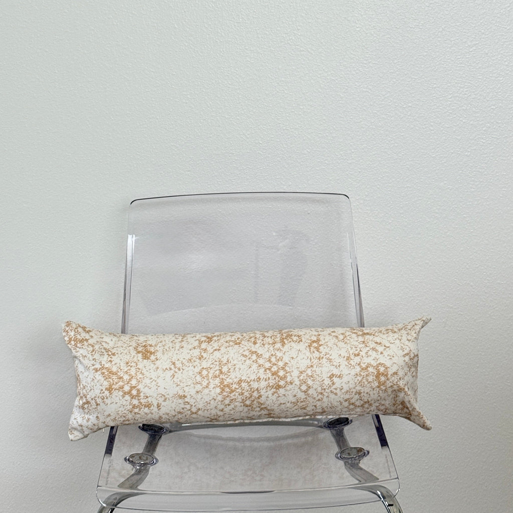 Decorative pillow with a beige and yellow pattern on a clear chair against a white wall.