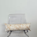 Decorative pillow with a beige and yellow pattern on a clear chair against a white wall.