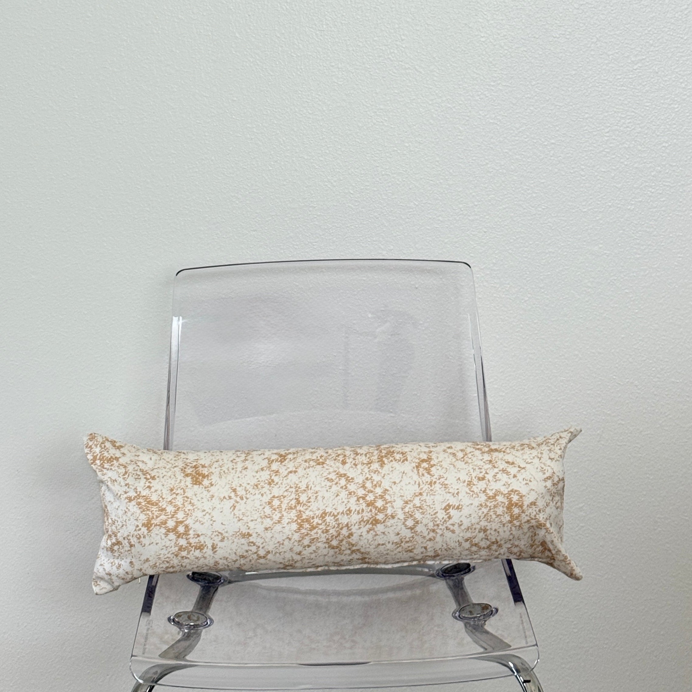 Decorative pillow with a beige and yellow pattern on a clear chair against a white wall.