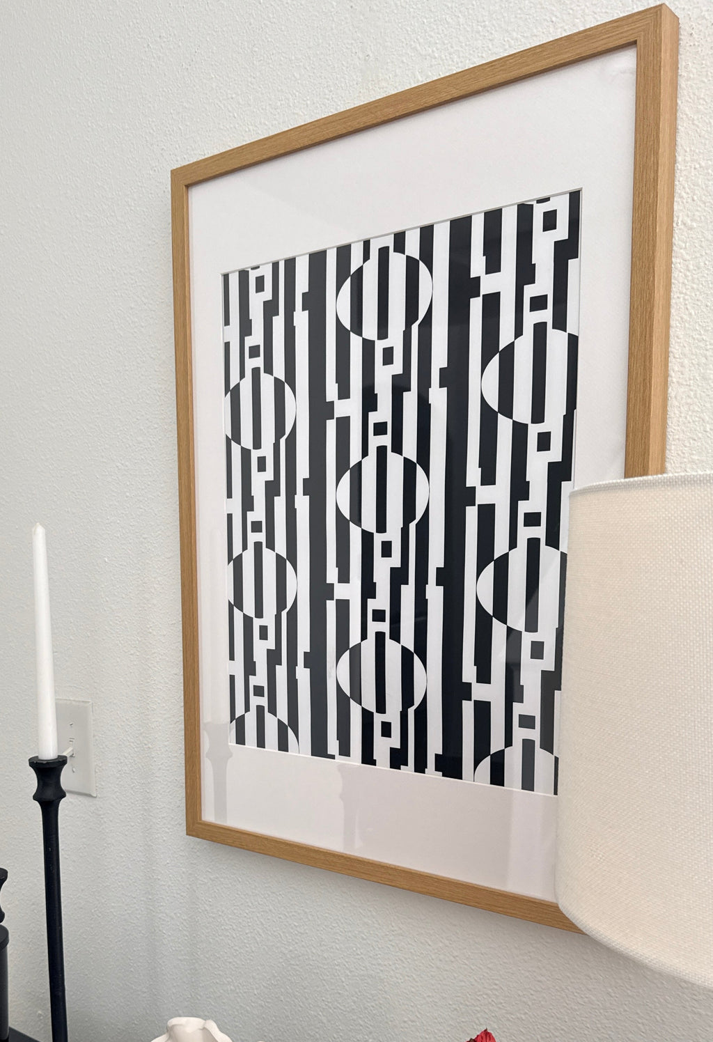 Framed black and white abstract art on a wall with candles, shell, and flowers on a table.