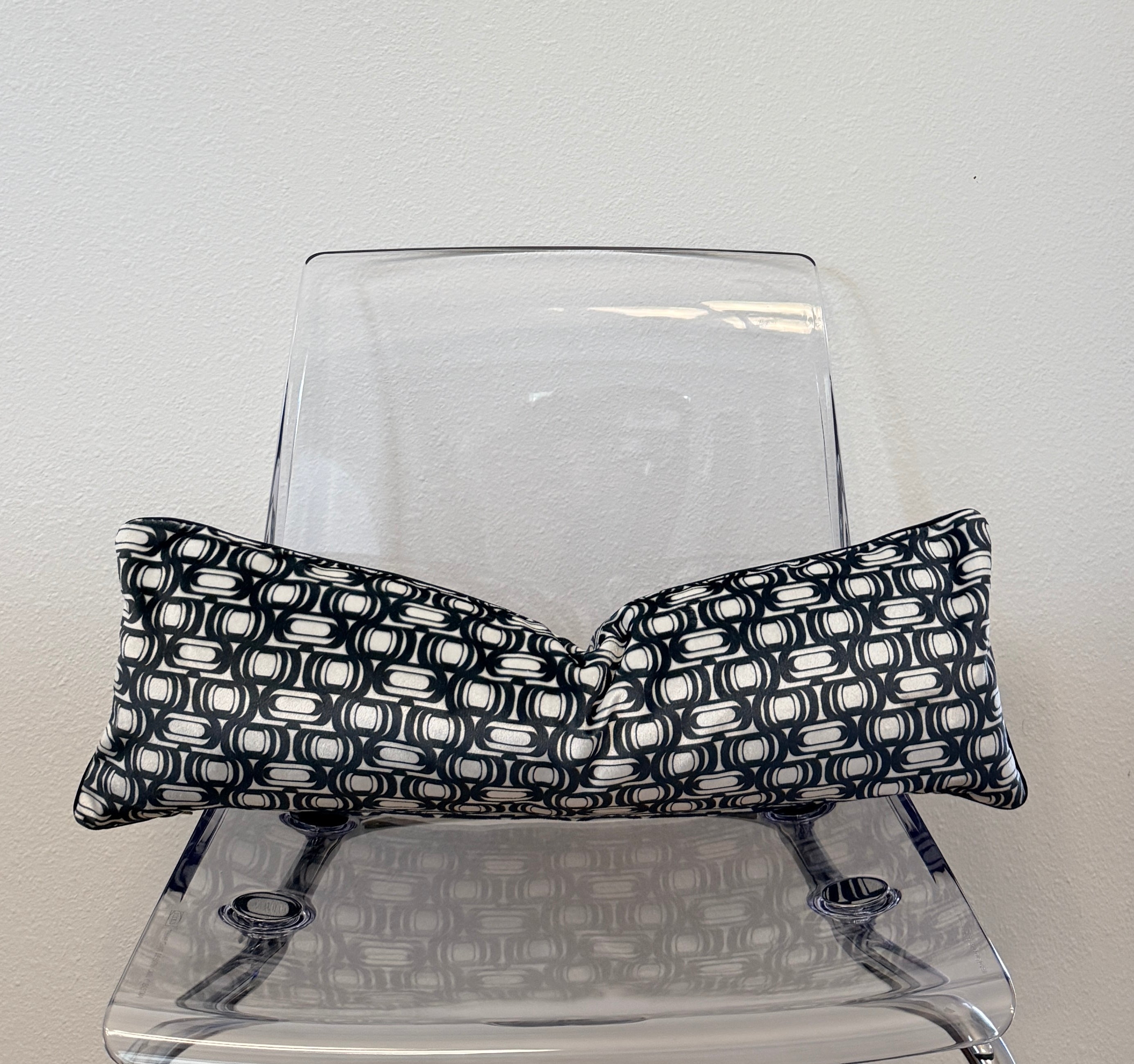 Black and white patterned pillow on a clear plastic chair against a light gray background