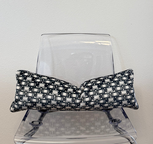 Black and white patterned pillow on a clear plastic chair against a light gray background
