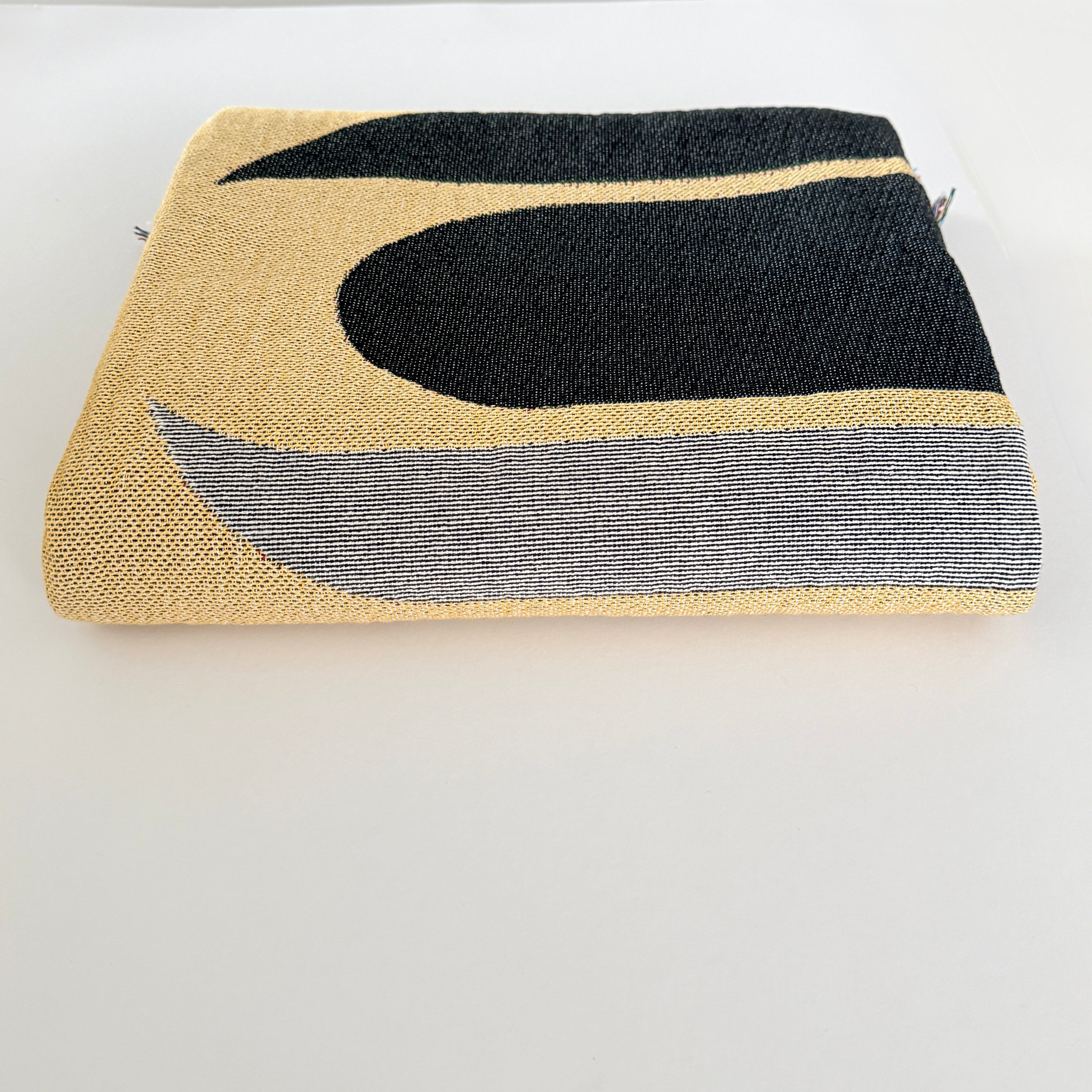Three-tone woven tapestry or blanket with gold, black, and white art design  folded on white background