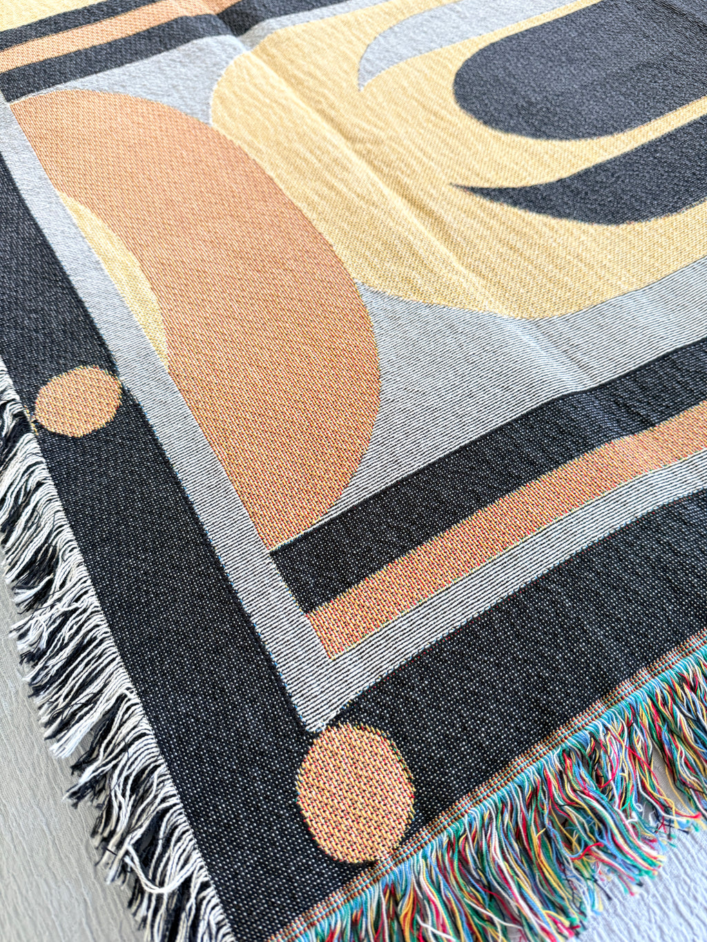 Close-up of a woven blanket with abstract patterns and fringes.