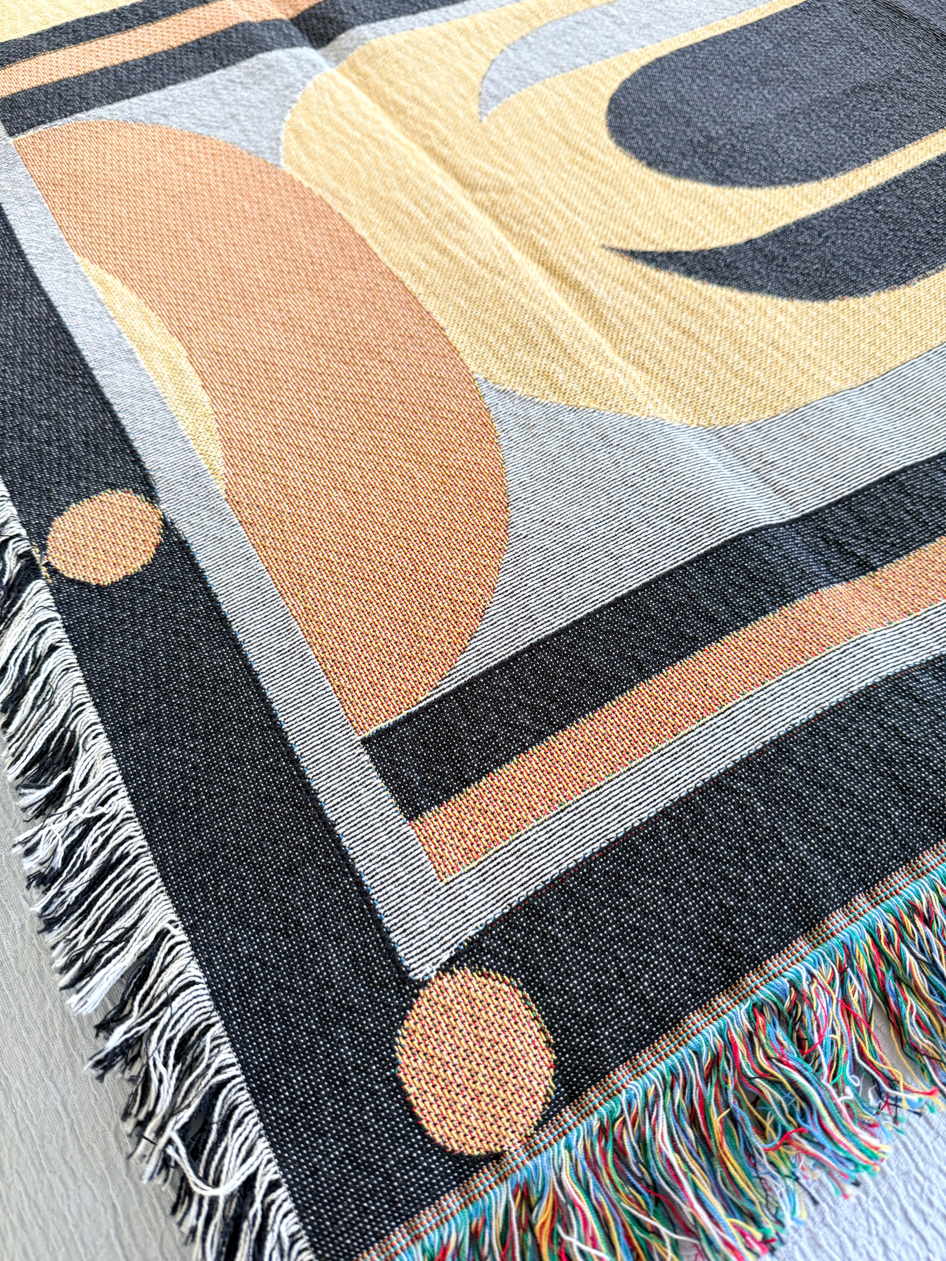 Close-up of a woven blanket with abstract patterns and fringes.