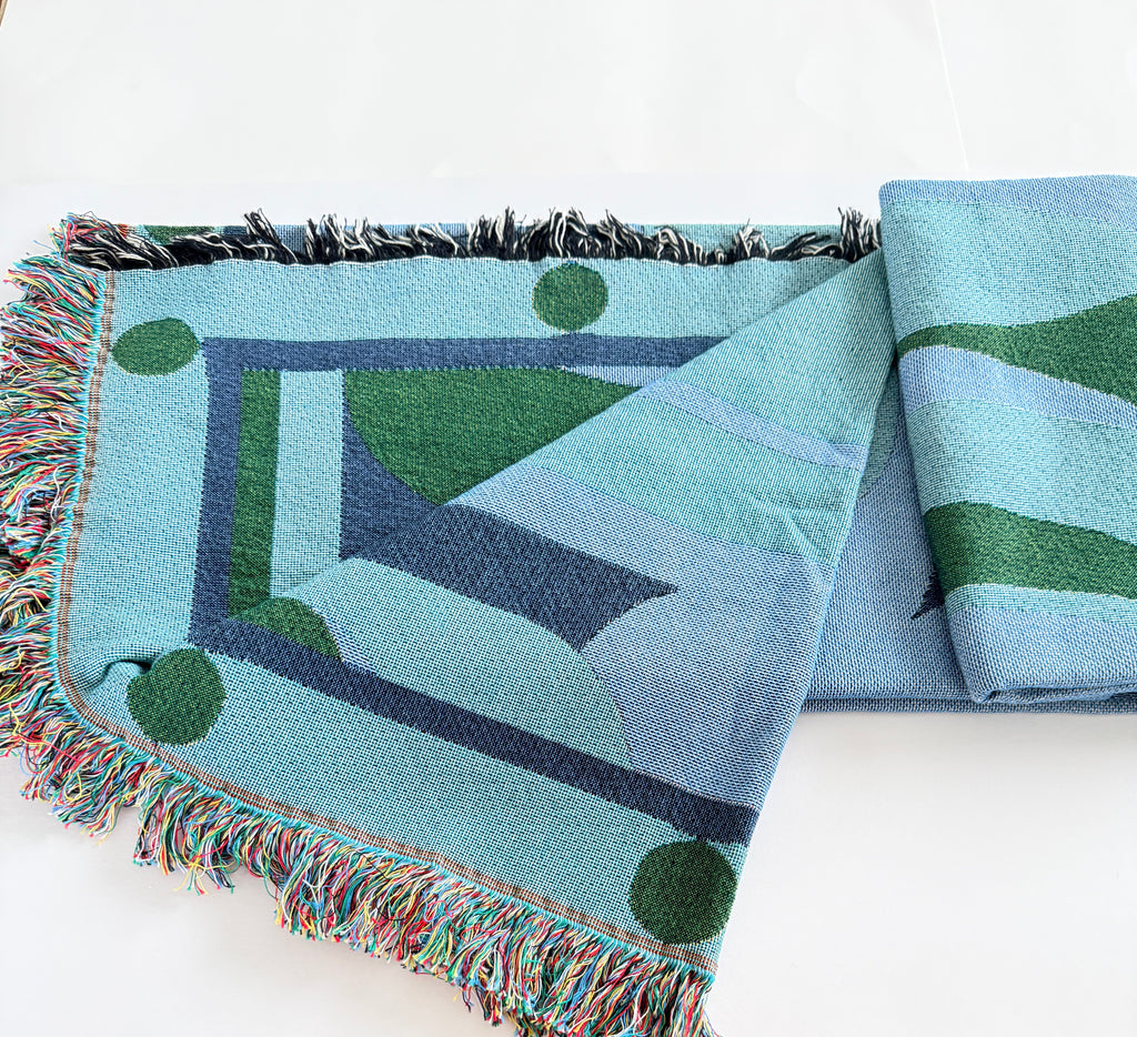 Woven green and blue blanket with geometric pattern on a white background