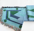 Woven green and blue blanket with geometric pattern on a white background