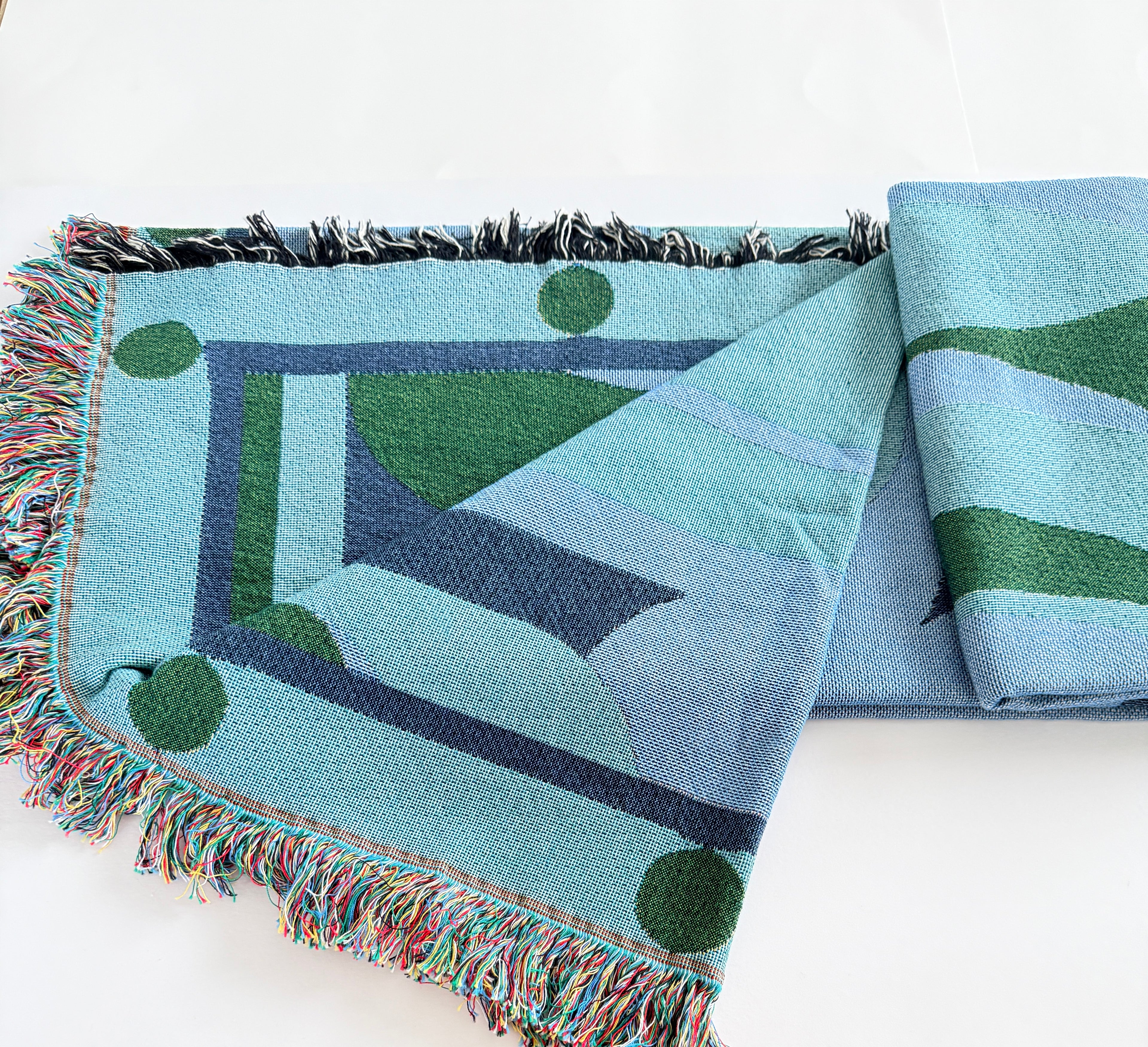 Woven green and blue blanket with geometric pattern on a white background