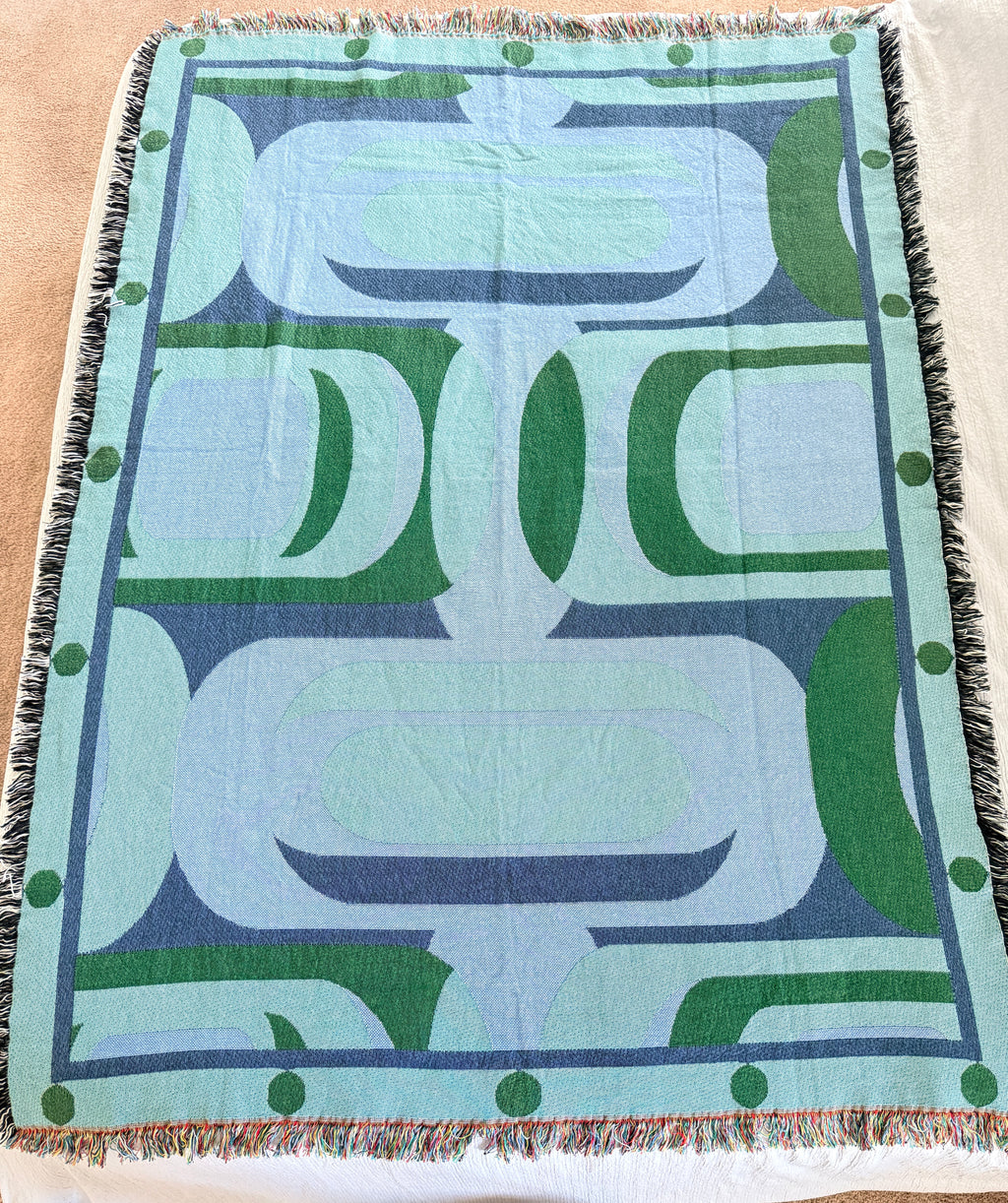 Decorative throw blanket with abstract patterns in green and blue on a light surface