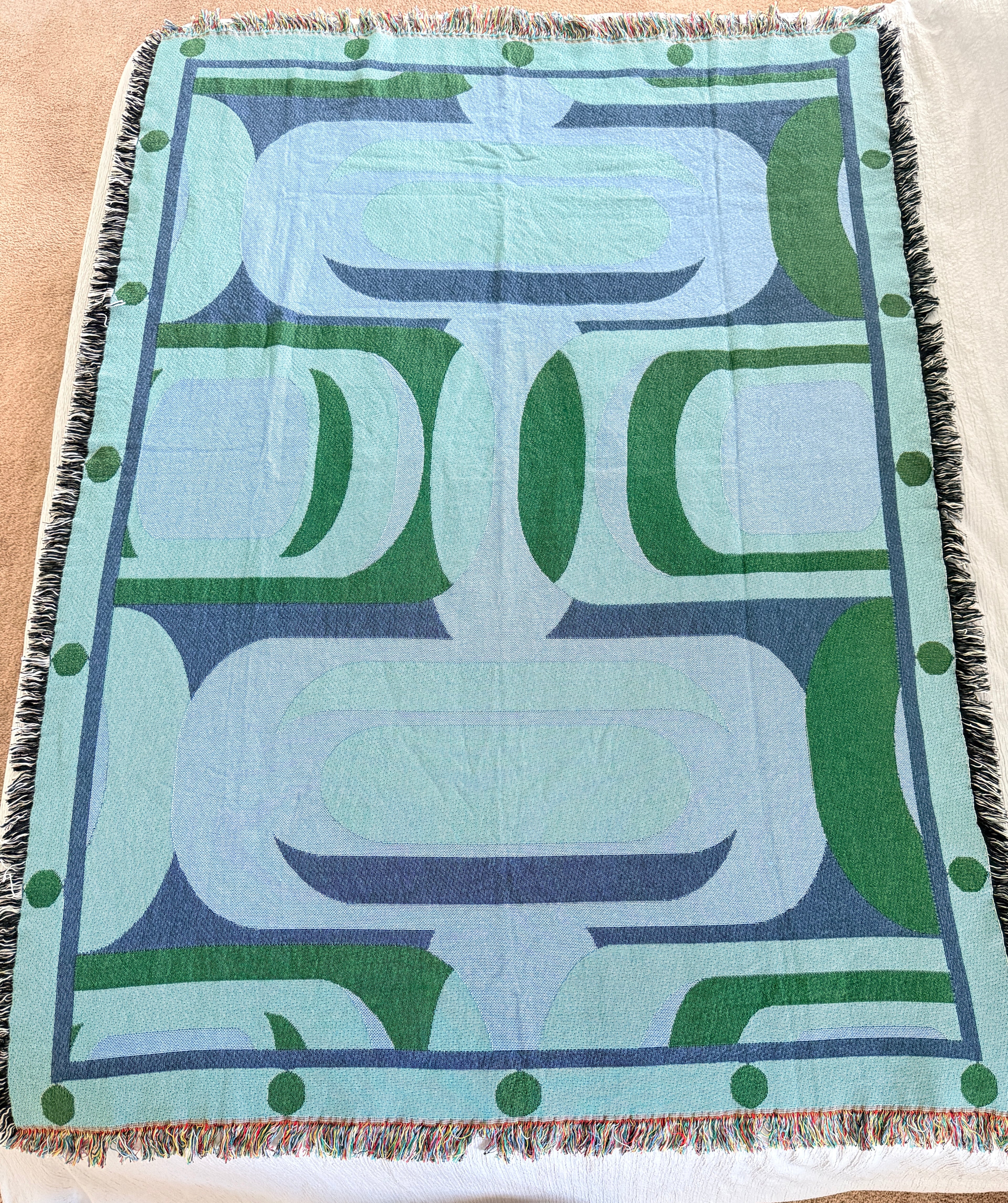 Decorative throw blanket with abstract patterns in green and blue on a light surface