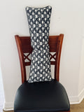 Black and white long lumbar pillow sitting vertically in chair against white wall 