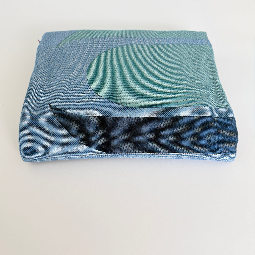 Folded woven blanket with blue and green pattern on a white background