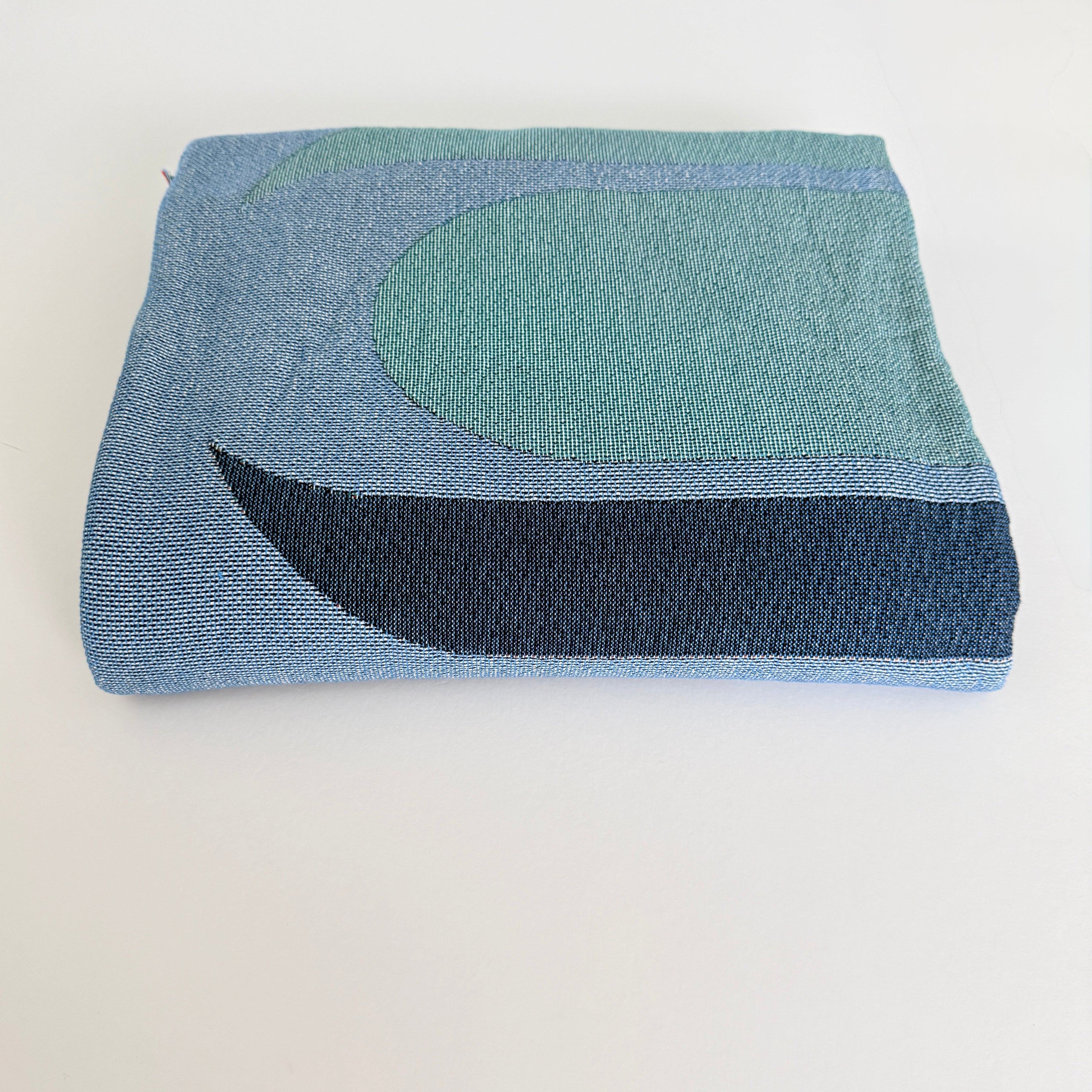 Folded woven blanket with blue and green pattern on a white background