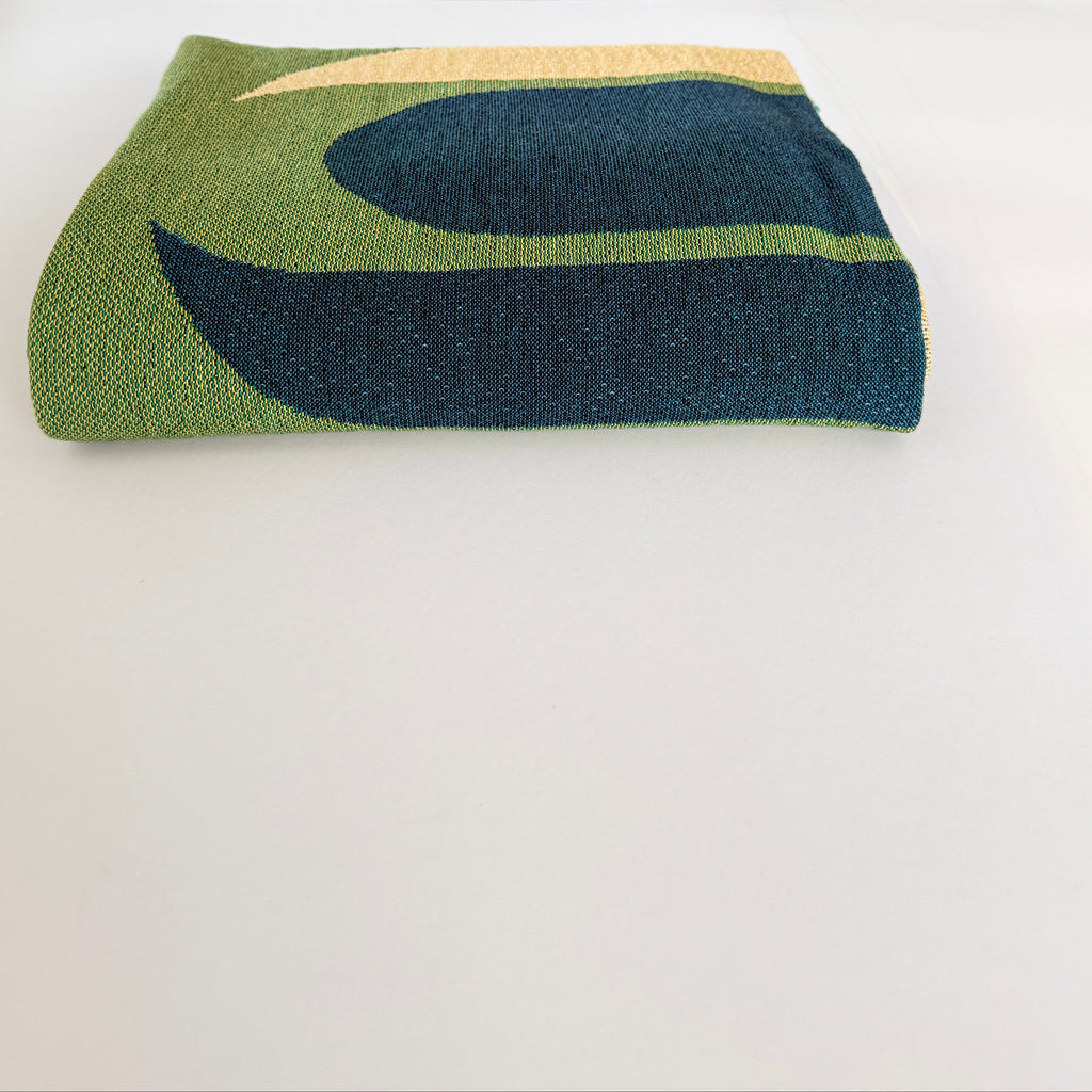 Folded blanket with green and blue abstract pattern on a white background