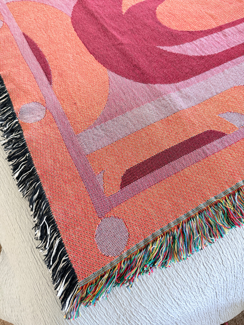 Close-up of a colorful woven blanket with geometric patterns on a white surface.