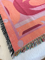 Close-up of a colorful woven blanket with geometric patterns on a white surface.