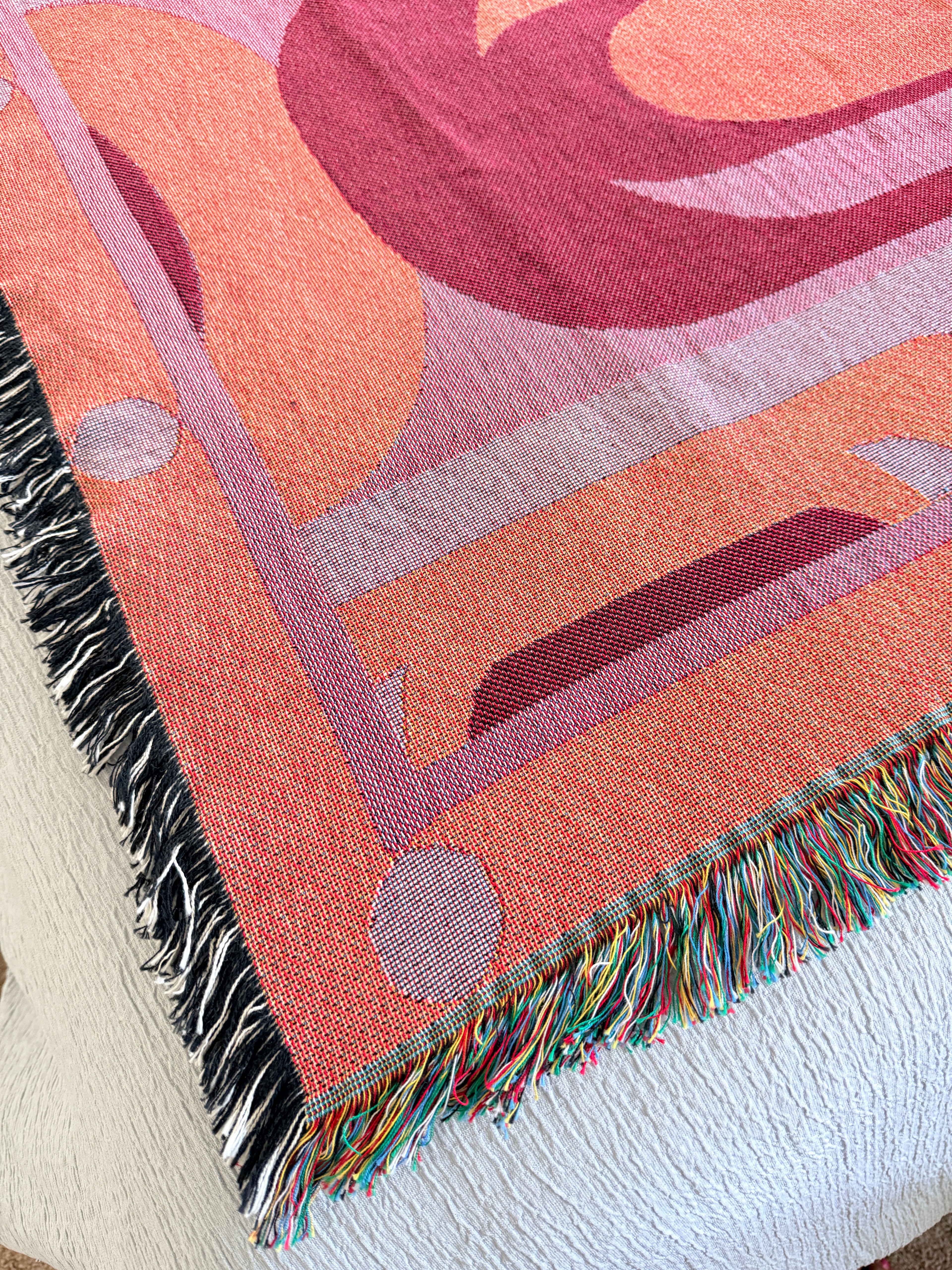 Close-up of a colorful woven blanket with geometric patterns on a white surface.
