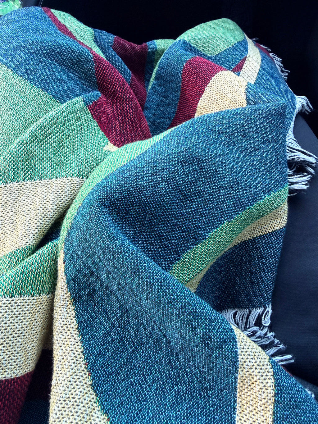 Multicolored woven throw blanket draped over person traveling in a car 