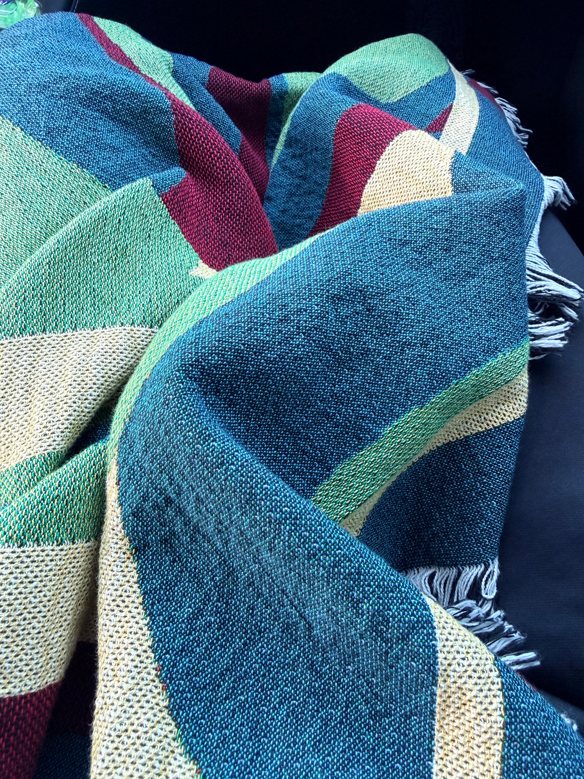 Multicolored woven throw blanket draped over person traveling in a car 