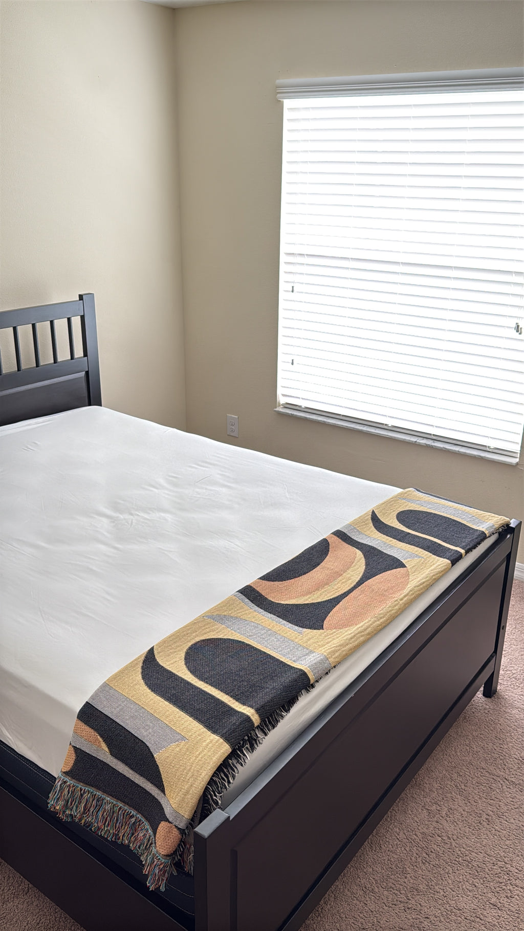 Abstract patterned black and yellow throw blanket draped over foot of queen sized dark bed with white sheets. 