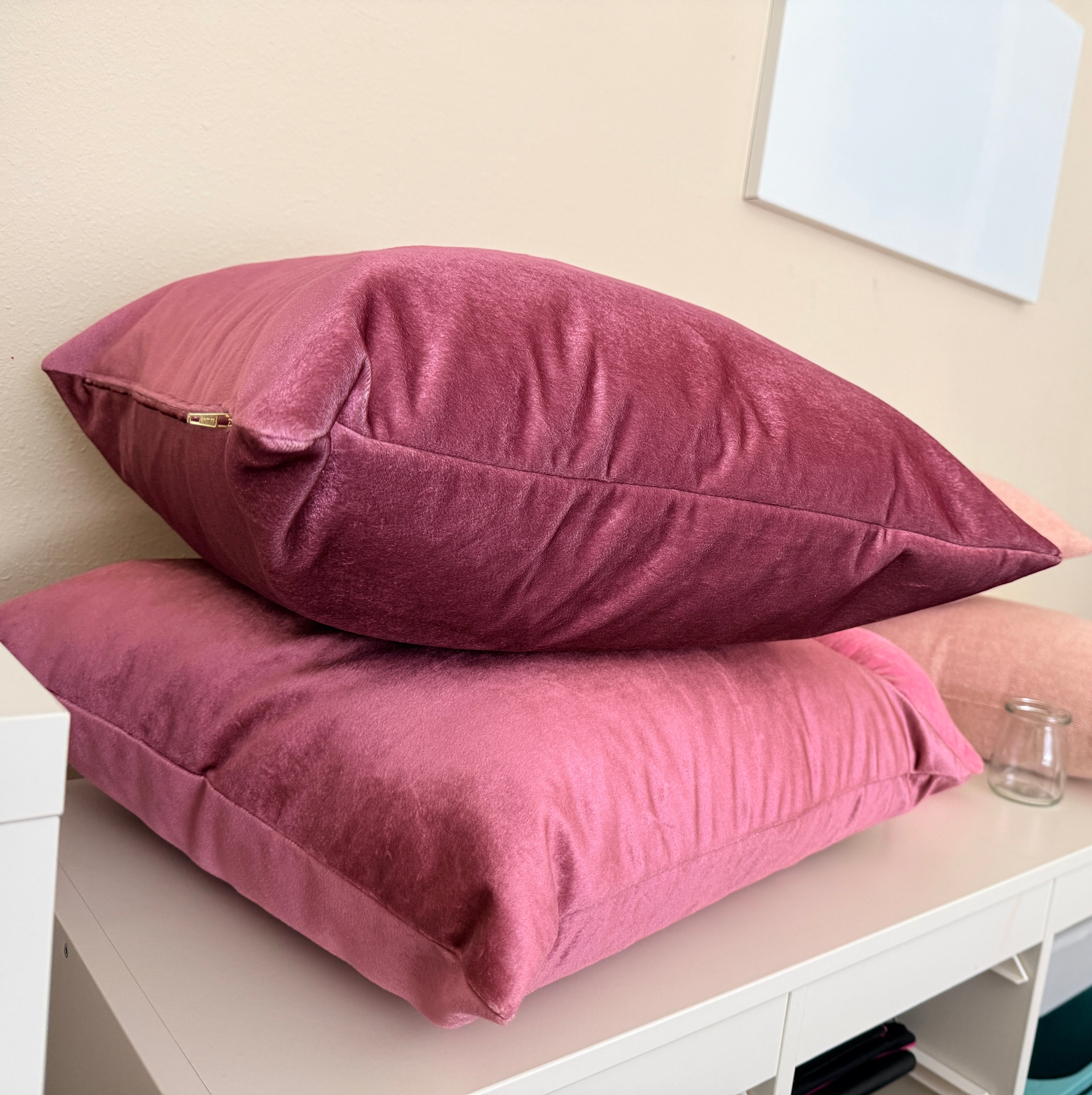 Two pink pillows stacked on a white surface with a neutral background